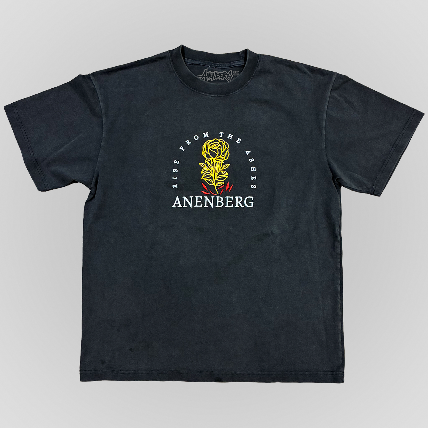 Front view of the Anenberg From the Ashes Tee featuring a vintage-washed charcoal black oversized T-shirt with a detailed embroidered golden yellow rose rising from red flames. White Rise From the Ashes lettering arches around the floral design, with the ANENBERG wordmark embroidered below. This heavyweight 7.5 oz boxy-fit T-shirt combines premium embroidery, a relaxed silhouette, and vintage-inspired Southern California streetwear styling.
