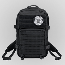 Front view of the Anenberg Black Out Pack Out Tactical Backpack featuring an all-black rugged design, multiple zippered storage compartments, MOLLE webbing, adjustable compression straps, and heavy-duty side-release buckles. A removable black-and-white Anenberg American Trade circular crest patch with the signature AB monogram accents the upper hook-and-loop panel. Padded shoulder straps, reinforced stitching, and tactical-inspired construction complete this versatile everyday carry backpack