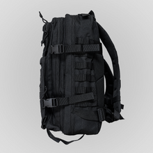 Left side view of the Anenberg Black Out Pack Out Tactical Backpack featuring rugged all-black fabric, multiple zippered storage compartments, MOLLE webbing attachment loops, and two adjustable side compression straps with heavy-duty quick-release buckles. Padded mesh shoulder straps, reinforced stitching, and tactical-inspired construction provide functional everyday carry storage. Versatile black tactical backpack from Southern California streetwear brand Anenberg.