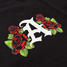 Close-up of the Anenberg Pit Crew Black Tee front chest graphic featuring a bold white Old English A logo surrounded by vibrant red roses and green leaves. Detailed screen-printed artwork on black fabric, showcasing Anenberg's California-inspired streetwear design.